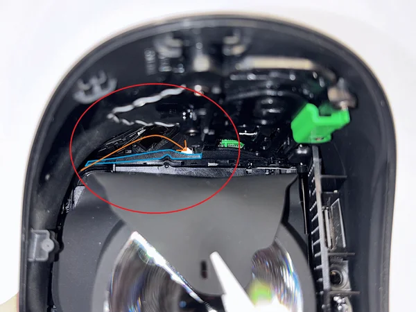 Plastic part marked in blue, with an orange arrow showing the cable path